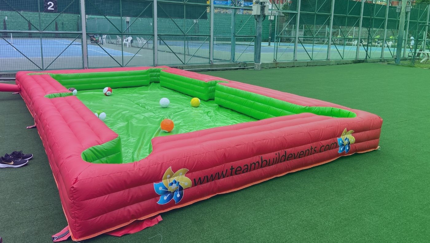 Players kick footballs into pockets on a giant inflatable pool table, combining two popular games for unique fun.